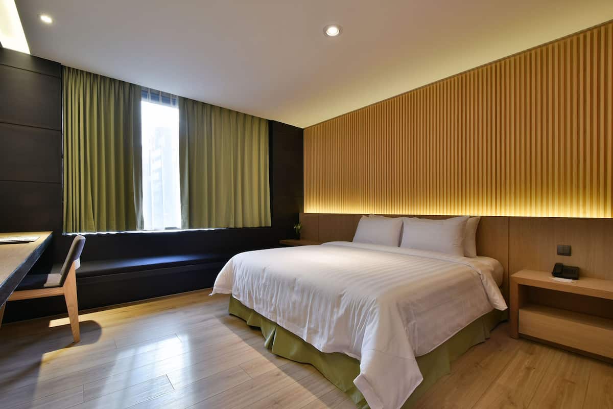 A modern hotel room with a large bed, a desk, and a window with curtains.