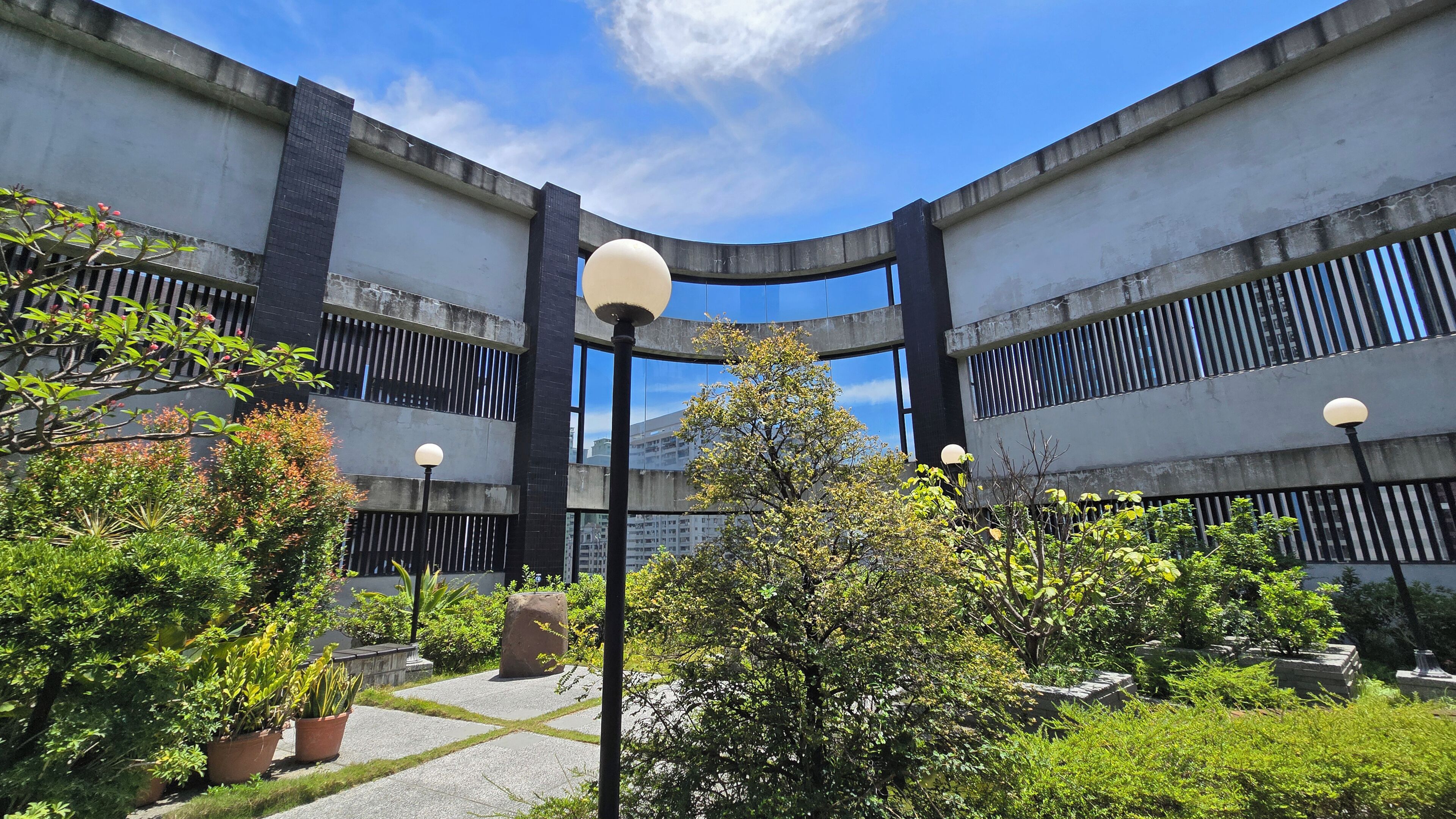 Un edificio con fachada curva, varios pisos y un patio con plantas en macetas y árboles.