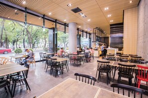 A spacious indoor dining area with multiple tables and chairs, large windows, and a modern ceiling design.