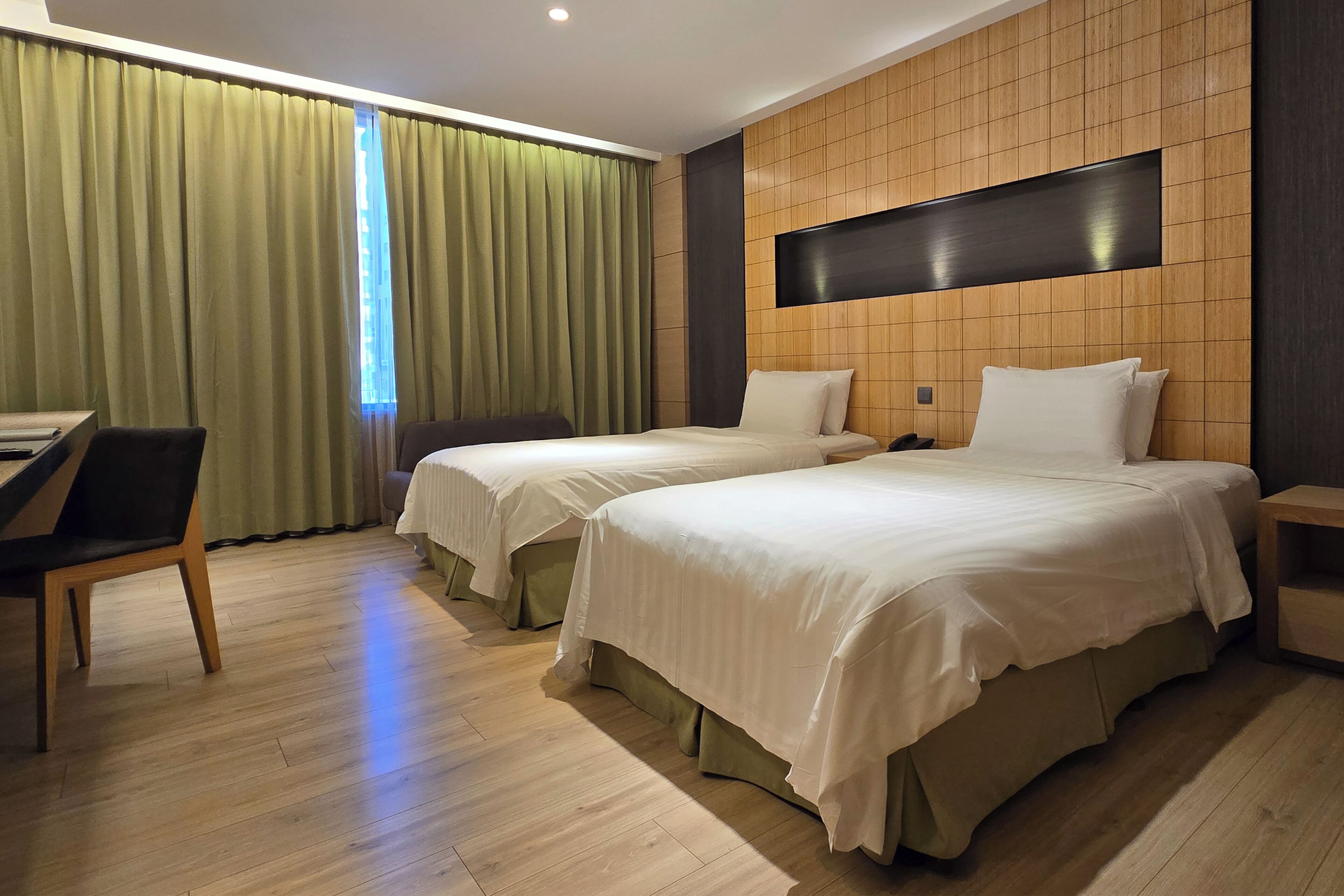 A hotel room with two beds, a desk, and a chair.