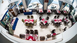 A dining area with multiple tables and chairs, a counter with a blue cloth, and a view of parked vehicles outside. - Diamond Crown Hotel (Yangon)