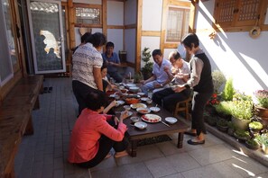 Un grupo de personas comiendo al aire libre en una mesa de madera con diversos platos.