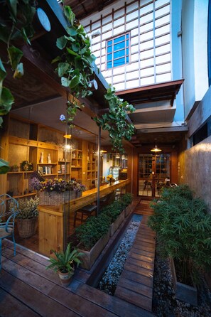 Ein traditionelles japanisches Interieur mit Holzböden, einem zentralen Holztisch und einem kleinen Gartenbereich mit Pflanzen und einem Pfad.