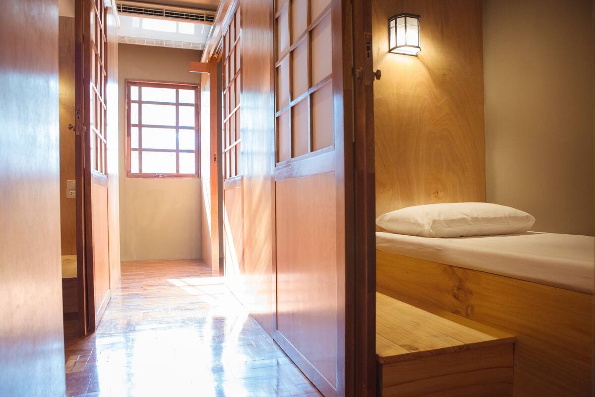Una habitación tradicional japonesa con puertas correderas, piso de madera, una cama con almohada blanca y un aplique de pared.