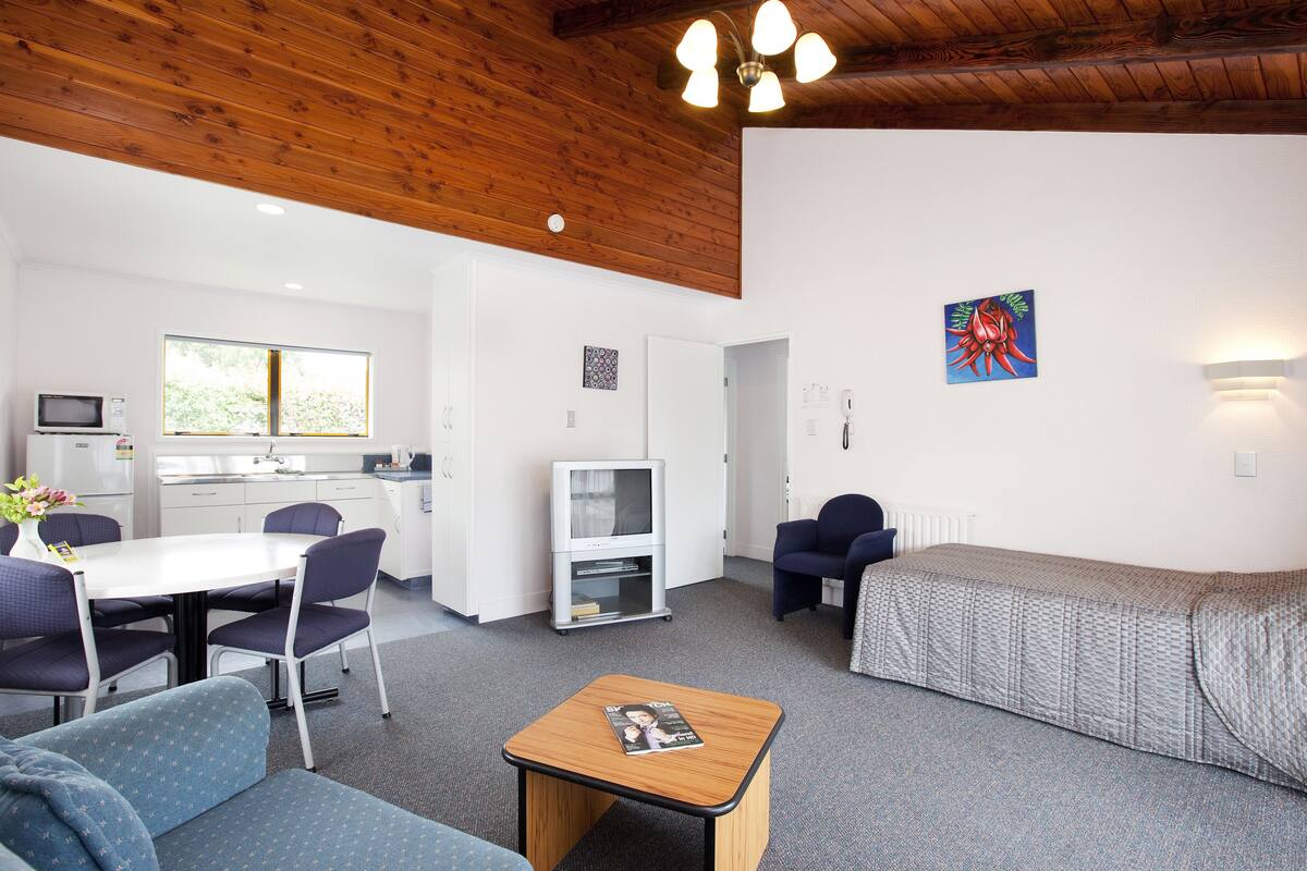 A modern room with a wooden ceiling, a dining area with a table and chairs, a sofa, a television, and a bed.