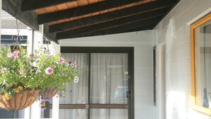 Ein blumengeschmückter Hängetopf, Holzboden, ein Fenster mit Vorhängen und eine Tür mit der Nummer 6.