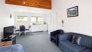 Ein modernes Hotelzimmer mit Holzboden, einem Essbereich mit Tisch und Stühlen, einer Sitzecke, einem Fernseher und einer Küchenzeile.