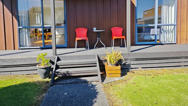 Ein modernes Gebäude mit überdachter Veranda, zwei roten Stühlen und einem kleinen Tisch.