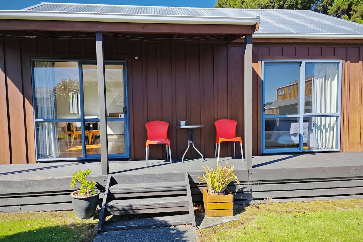 A modern building with a covered porch, two red chairs, and a small table.