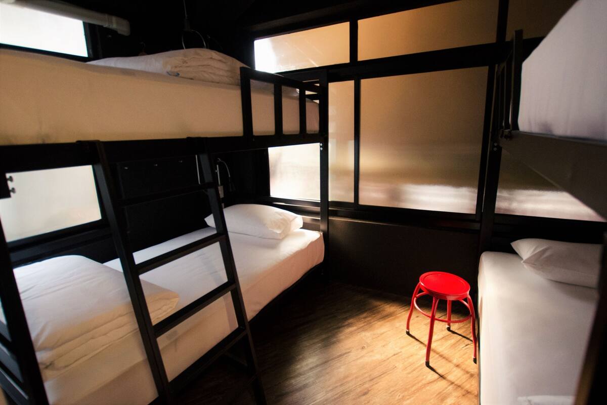 A bunk bed room with a red stool and wooden flooring.