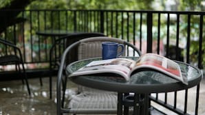 Una mesa con una revista y una taza azul, rodeada de sillas de mimbre y una barandilla de metal negro.