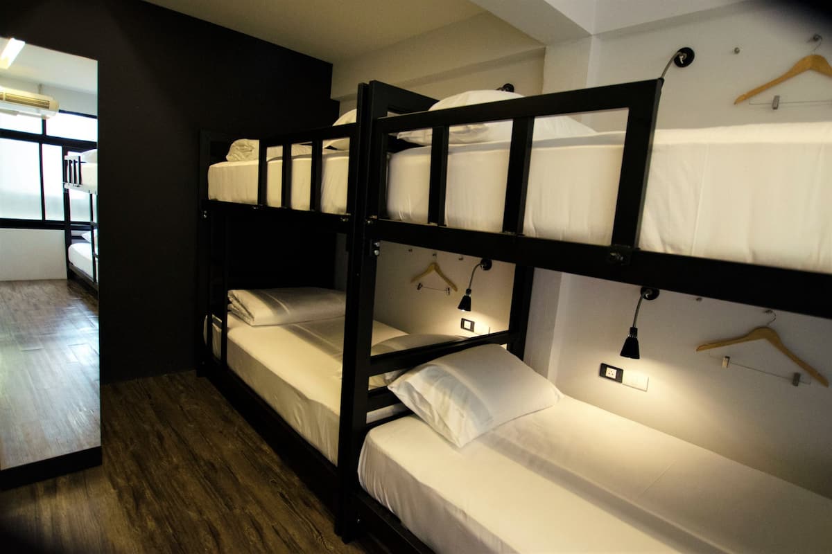 A bunk bed room with wooden frames, white bedding, and a wooden floor.