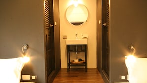 Un baño de hotel con suelo de madera, un espejo redondo y dos camas blancas con iluminación.