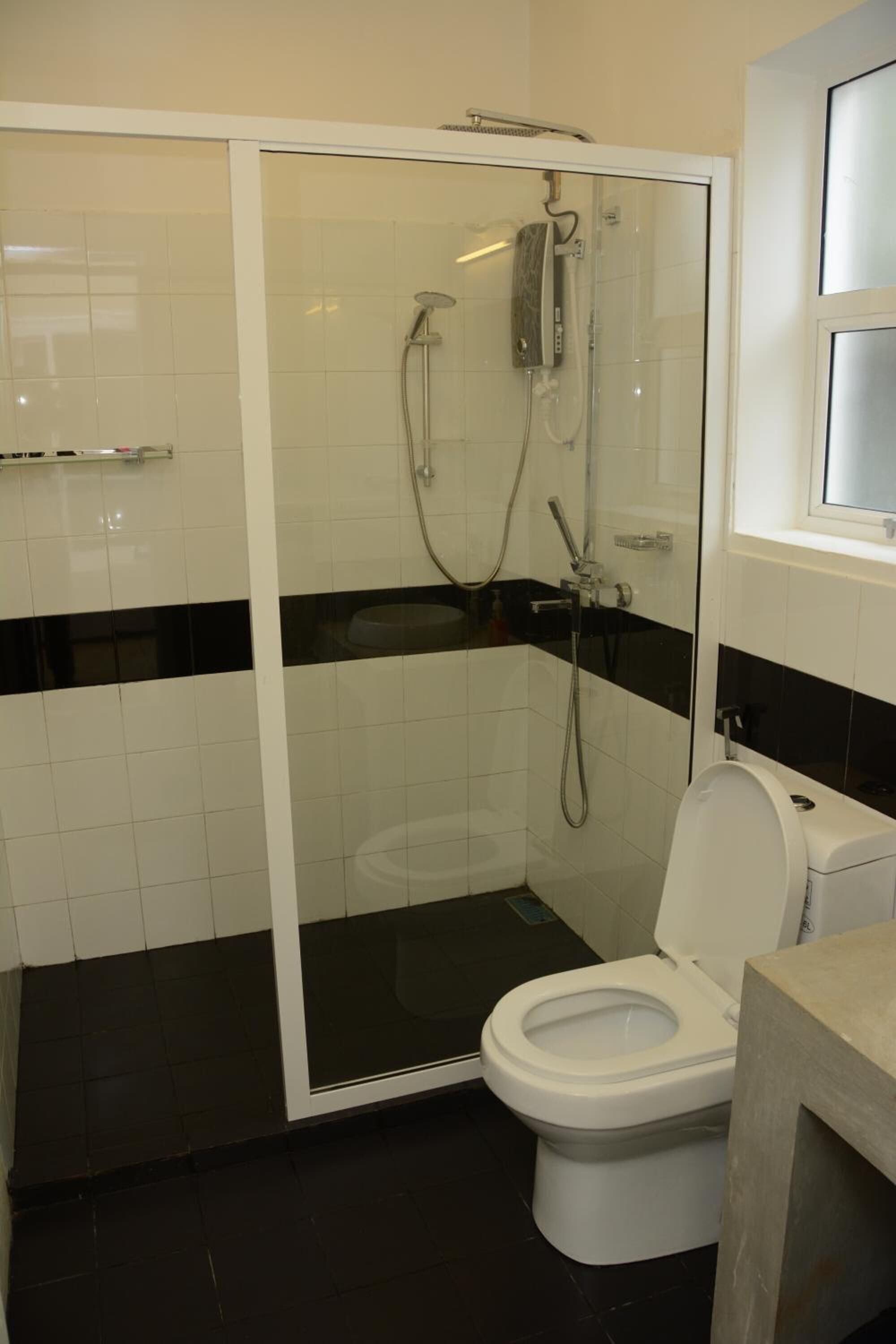 Ett badrum med en dusch som är avskärmad med glasväggar, en vit toalett och ett svart- och vitrutigt golv.