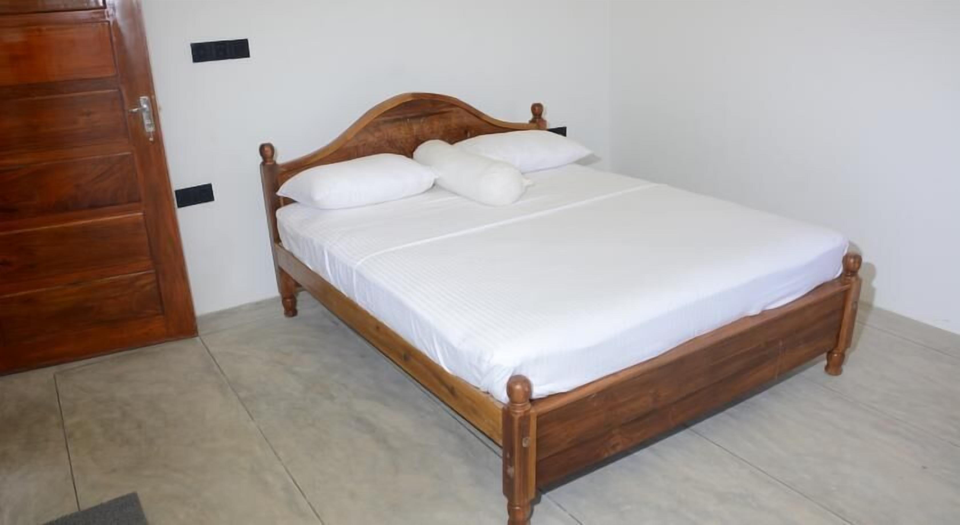 Una cama de madera con ropa de cama blanca en una habitación con suelo de baldosas y un armario de madera.