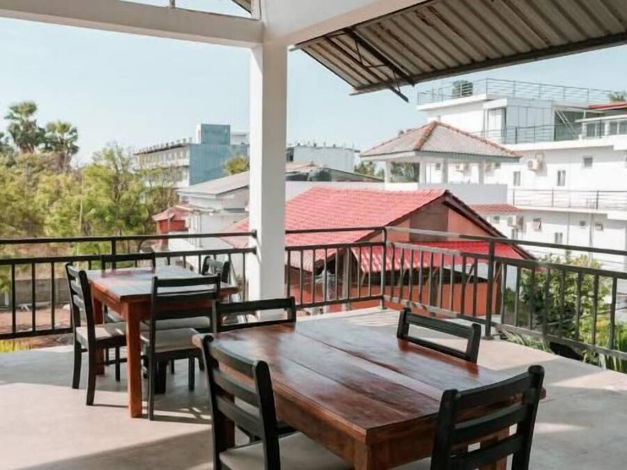 An outdoor patio with wooden tables and chairs, a metal railing, and a view of buildings in the background.