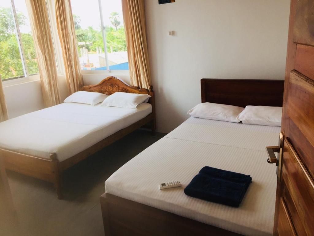 A hotel room with two single beds, a wooden headboard, a window with curtains, and a door.