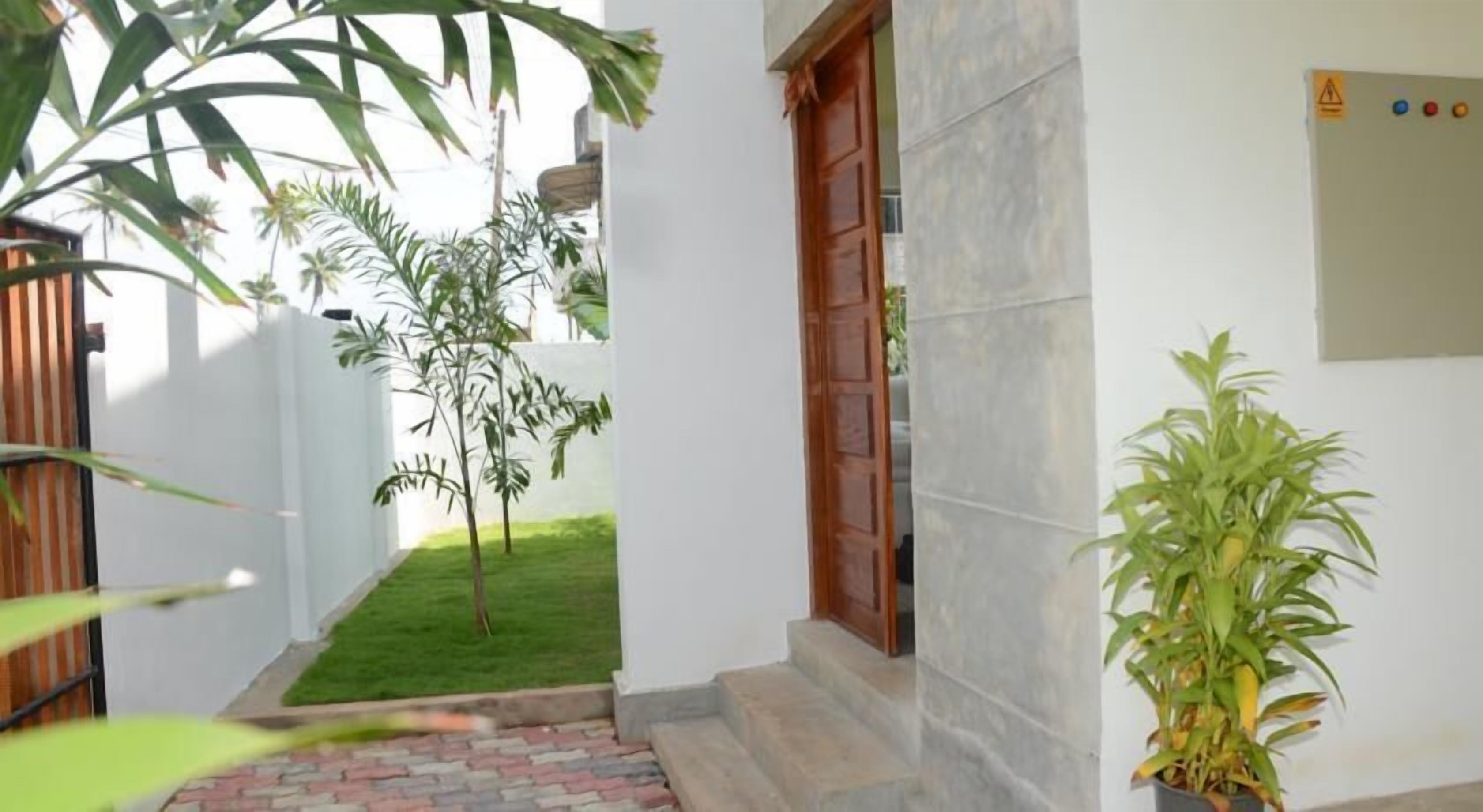 Un sendero estrecho que conduce a una puerta de madera, flanqueado por paredes blancas y una pequeña zona de césped.