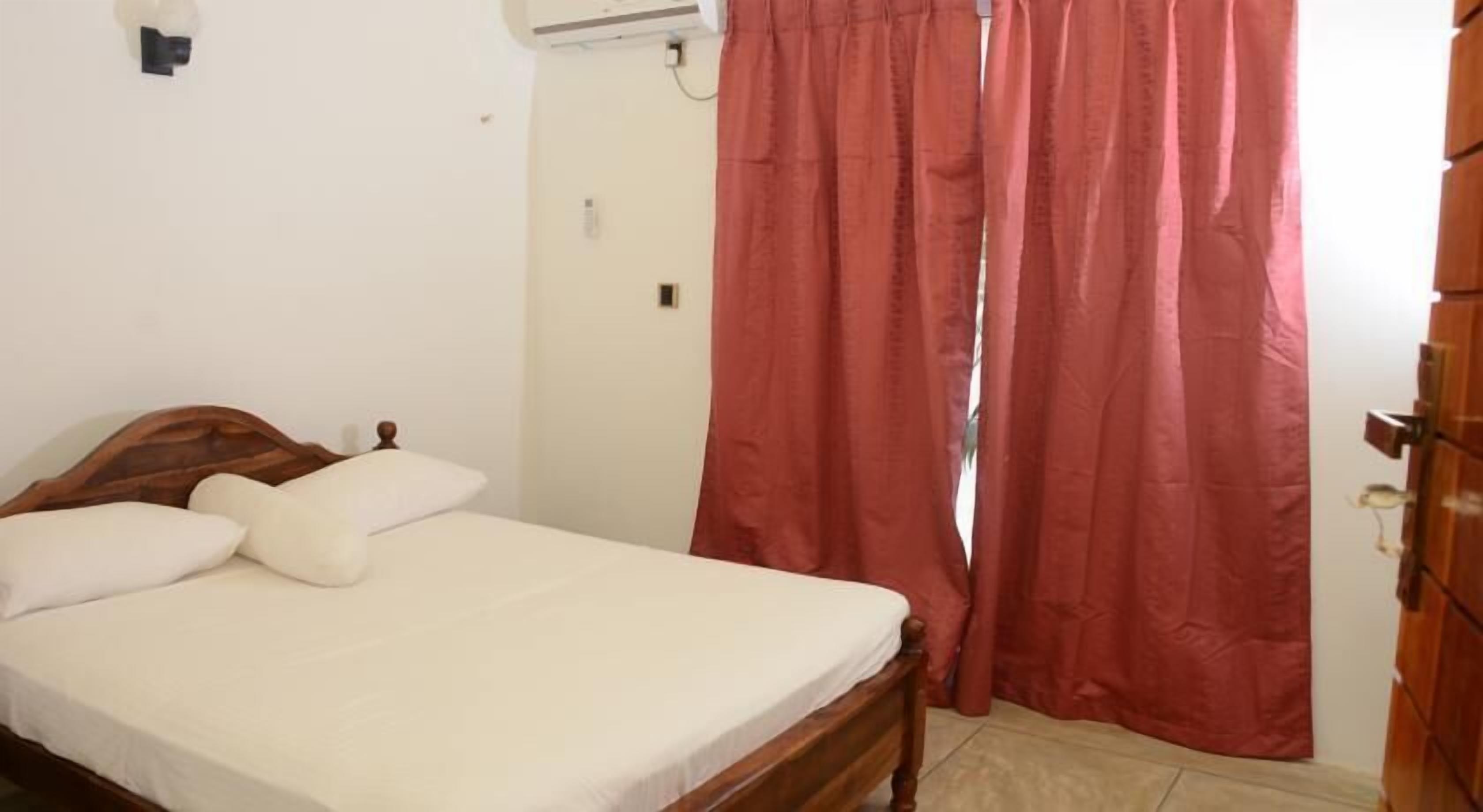 Une chambre à coucher avec un lit en bois, du linge de lit blanc, un rideau rouge et un appareil de climatisation fixé au mur.