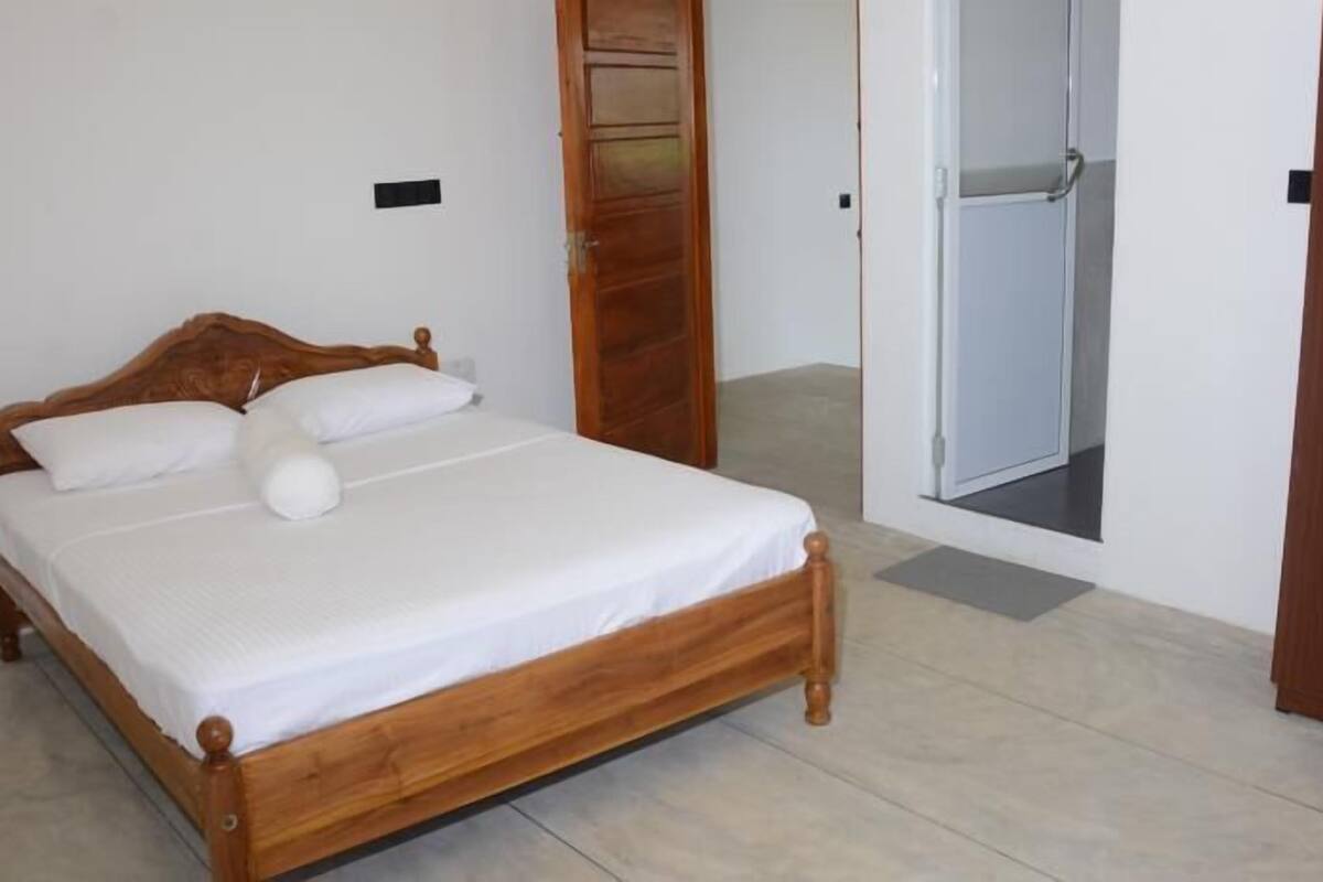 A single bed with a wooden headboard and white bedding in a room with white walls and a tiled floor.