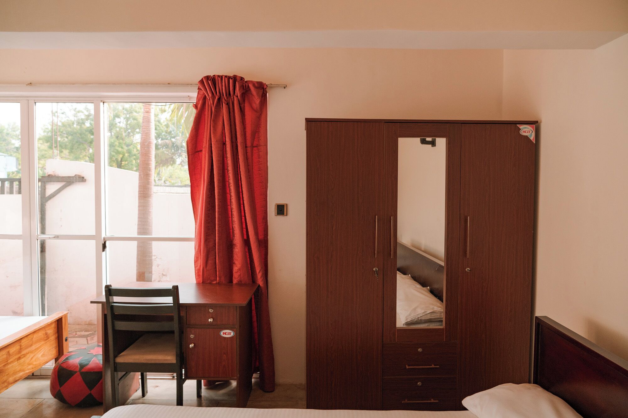 A bedroom with a wooden wardrobe, a desk, and a chair.