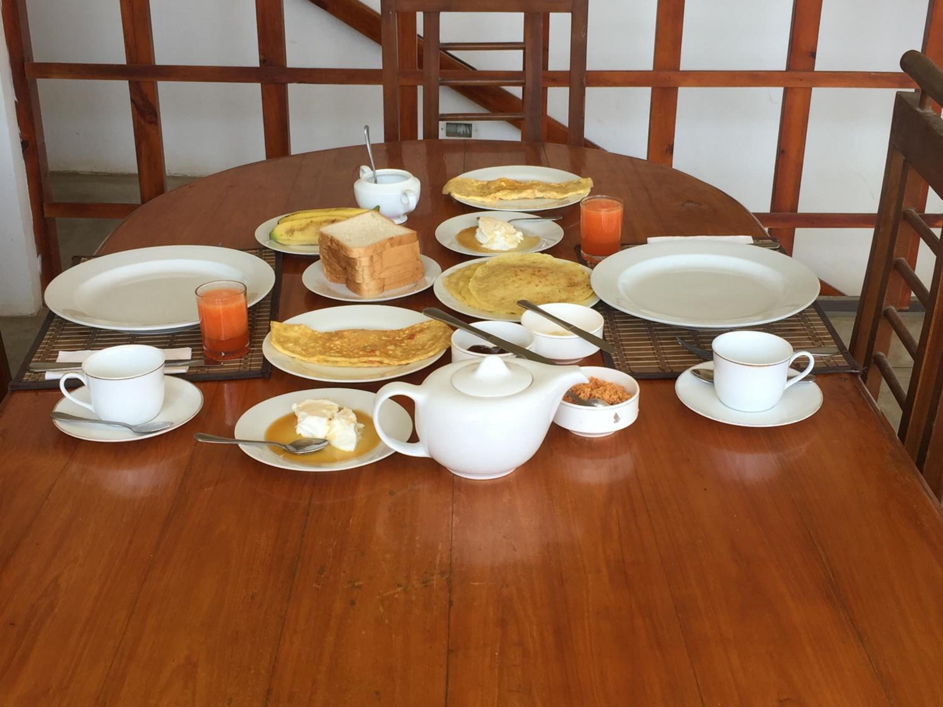 A wooden dining table set with plates, bowls, a teapot, and a glass of orange juice.