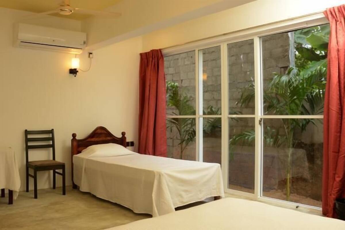 A bedroom with a single bed, a chair, a window with curtains, and an air conditioning unit.