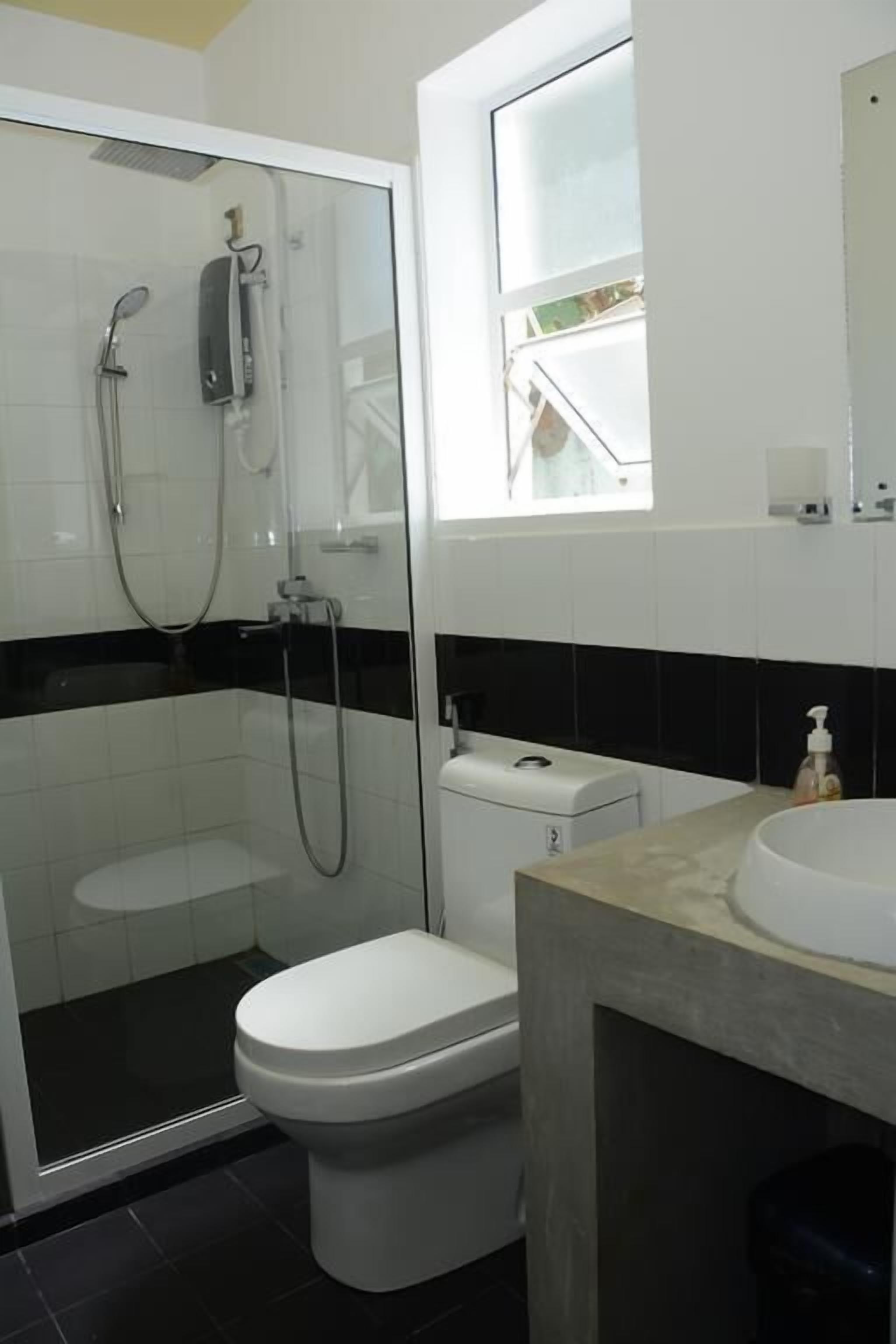 Un baño con ducha de vidrio, inodoro blanco y lavamanos con espejo superior.