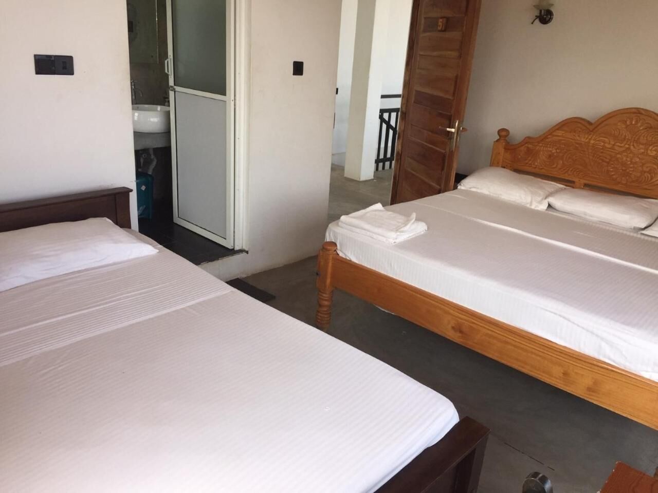 Una habitación con dos camas individuales, cabecera de madera, pared blanca y una puerta que da a un baño.