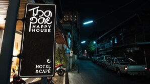 A sign for "The One Happy House Hotel & Café" with a street view in the background. - Thapae Happy House (Chiang Mai)