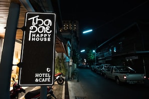 A sign for "The One Happy House Hotel & Café" with a street view in the background. - Thapae Happy House (Chiang Mai)