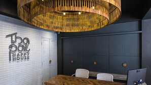 A modern office space with a herringbone wood table, a large hanging wooden light fixture, and a wall with the text "The House Happy House". - Thapae Happy House (Chiang Mai)