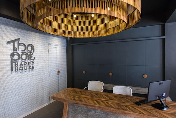 A modern office space with a herringbone wood table, a large hanging wooden light fixture, and a wall with the text "The House Happy House".