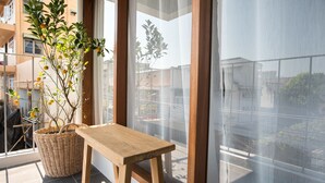 A balcony with a wicker basket holding a plant, a wooden stool, and a view of a building through a glass door. - Thapae Happy House (Chiang Mai)