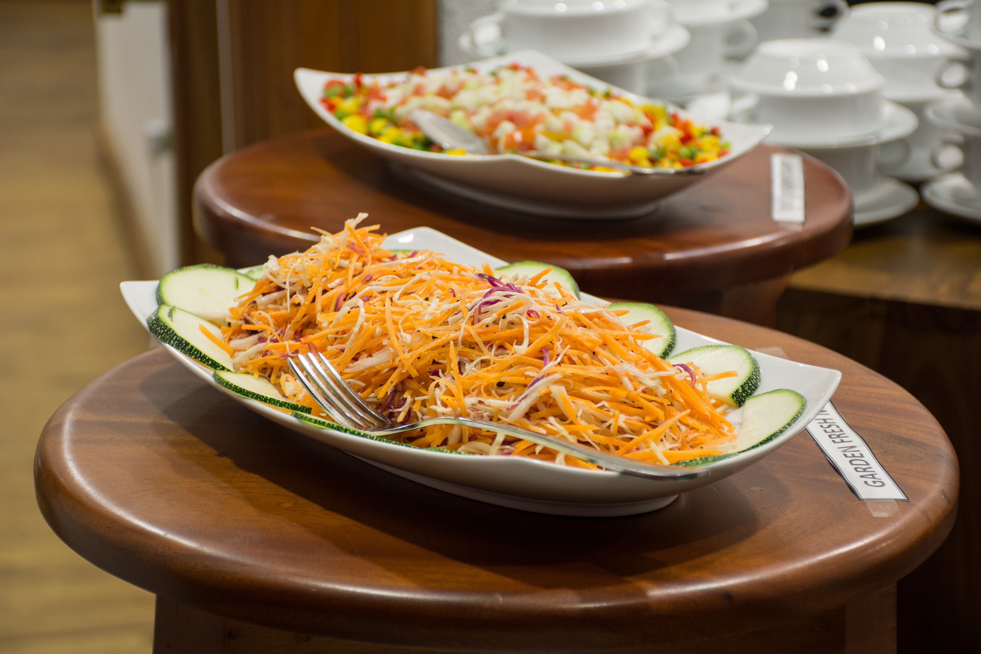 Una mesa de buffet con una variedad de platos, incluyendo una ensalada de zanahoria rallada y pepino, y una ensalada mixta de verduras.