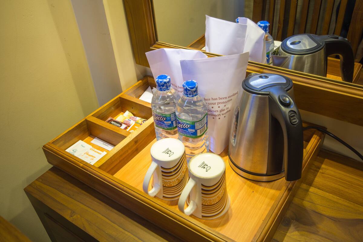 Minibar de una habitación de hotel con una bandeja que contiene tazas de café, botellas de agua, una tetera y una caja de pañuelos.