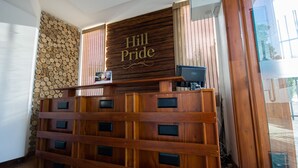 A reception desk with a sign reading "Hill Pride" and a wooden panel wall with logs. - Hill Pride City Hotel (Nuwara Eliya)