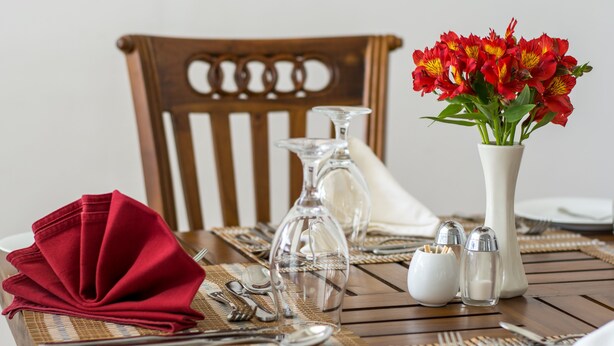 A dining table set with a red napkin, clear glassware, and a white vase with red flowers. - Hill Pride City Hotel (Nuwara Eliya)