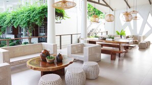 A spacious outdoor seating area with wicker furniture, a wooden table with a vase and plants, and hanging wicker lamps. - Paras Beach Resort (Mambajao)