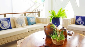 A bright living area with a wicker sofa, a wooden coffee table, and decorative items including a vase and a potted plant. - Paras Beach Resort (Mambajao)
