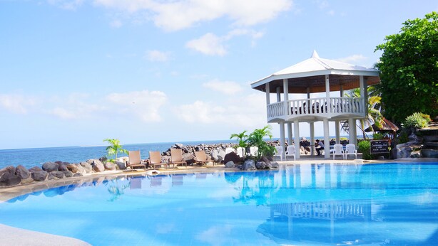 A pool with a gazebo, lounge chairs, and a view of the ocean. - Paras Beach Resort (Mambajao)