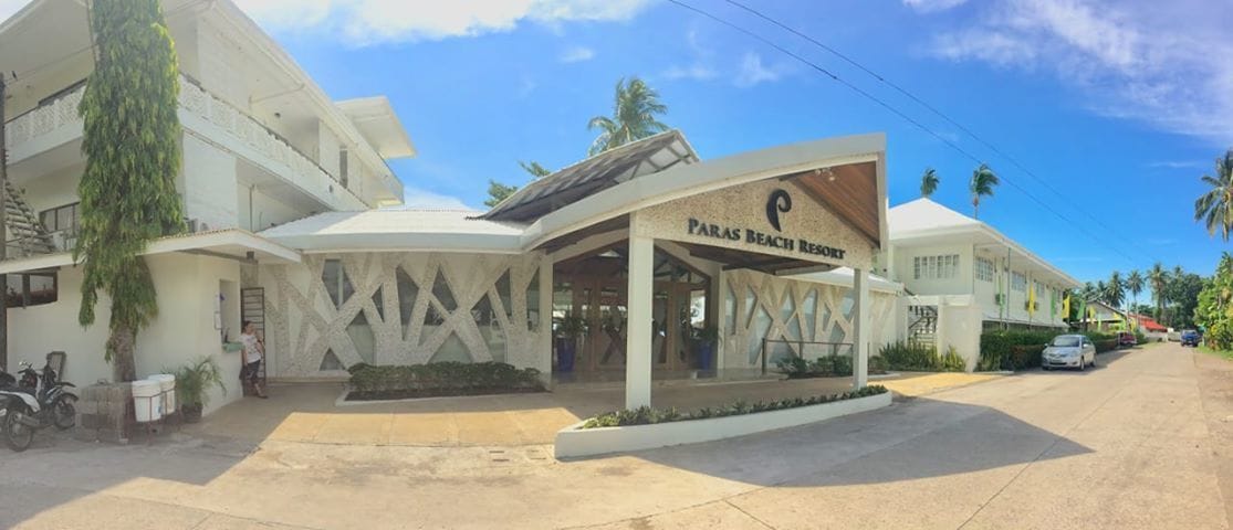 Un resort con entrada techada, palmeras y cielo despejado.