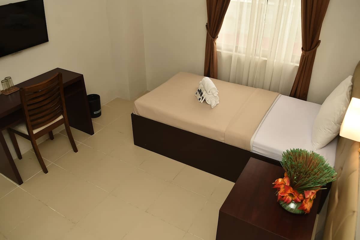 A compact hotel room with a bed, a desk, a chair, and a small table with a vase of flowers.