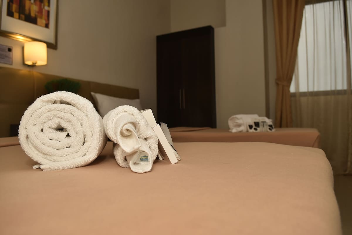 A hotel room with two beds, each with a rolled white towel and a white pillow.