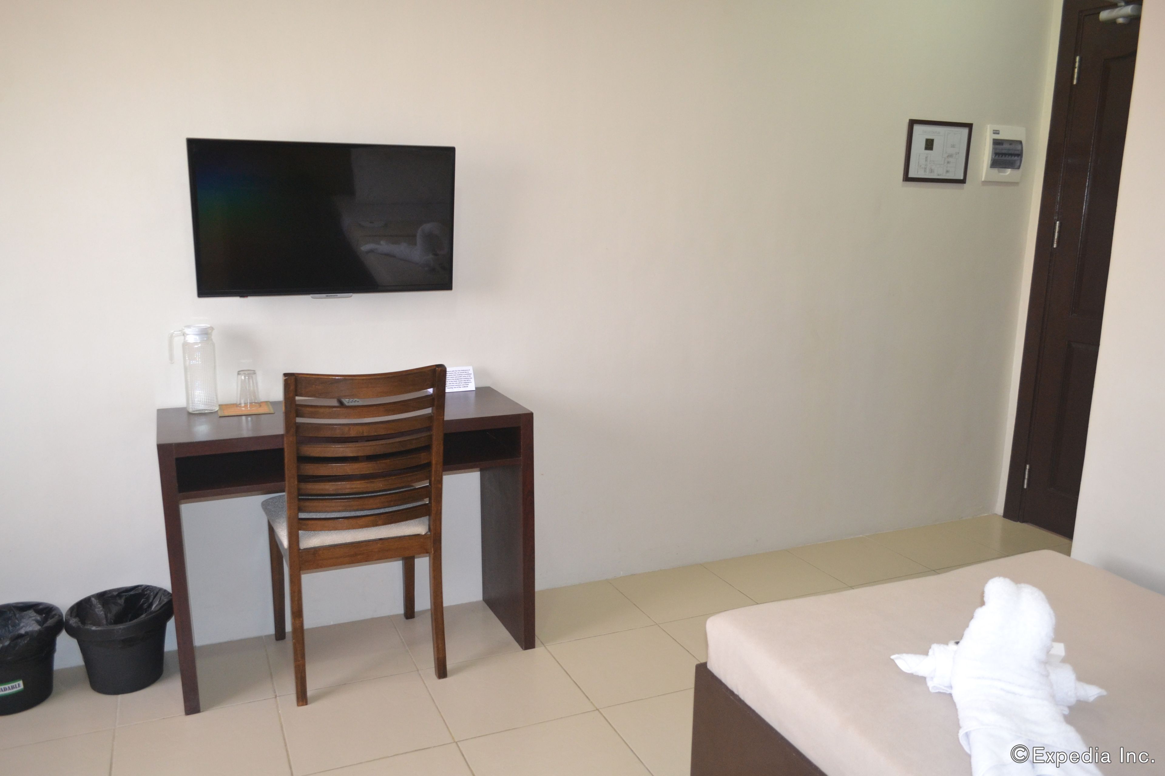 A hotel room with a bed, a desk with a chair, a television, and a trash bin.