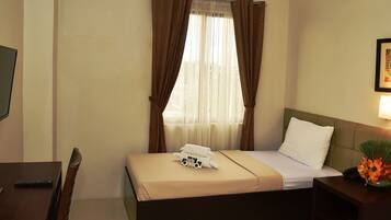 A hotel room with a bed, a bedside table with a lamp, a TV on the wall, and a window with curtains.