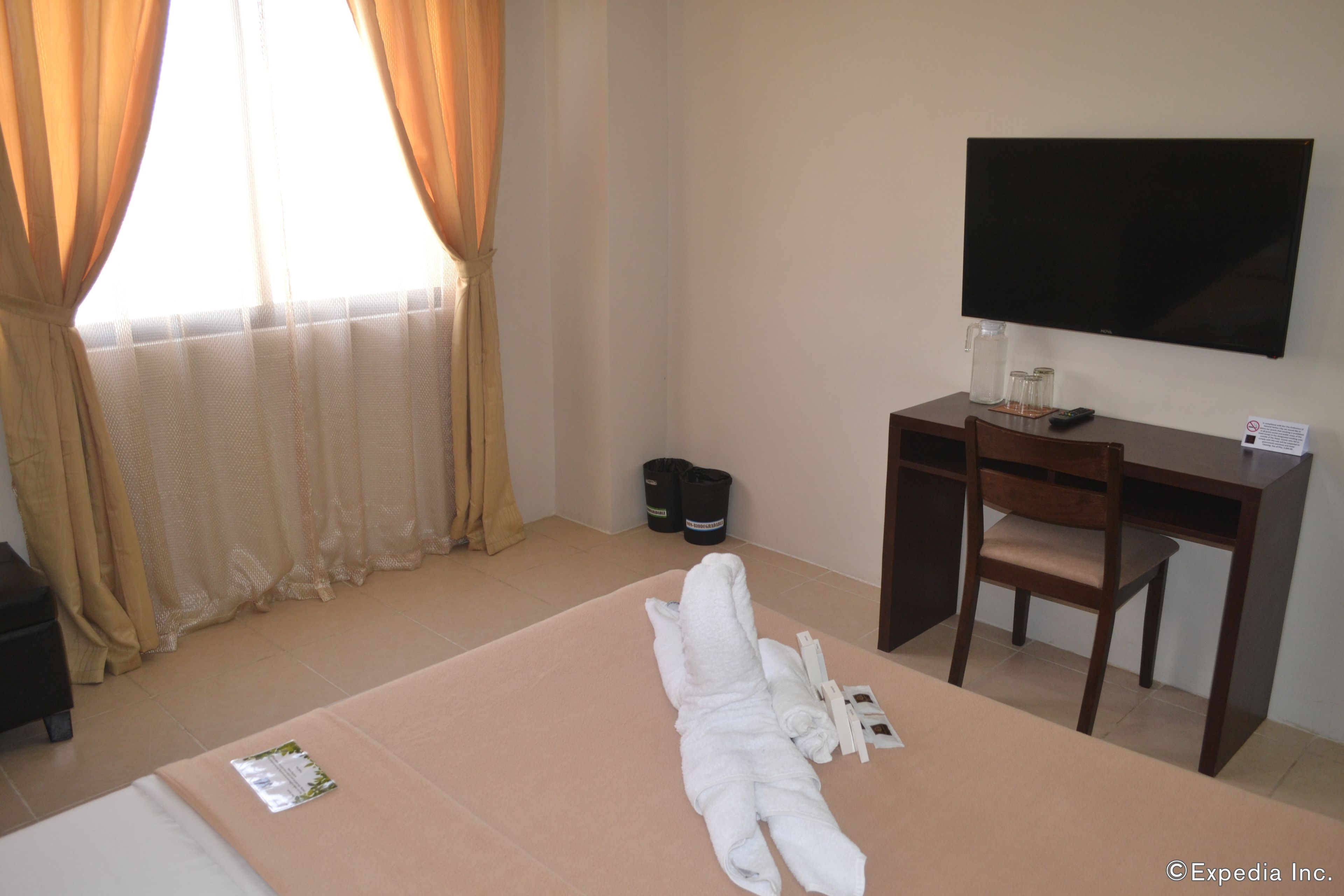 Una habitación de hotel con cama, escritorio, silla, televisión y ventana con cortinas.