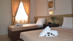 A hotel room with two beds, a nightstand, a lamp, and a window with curtains.