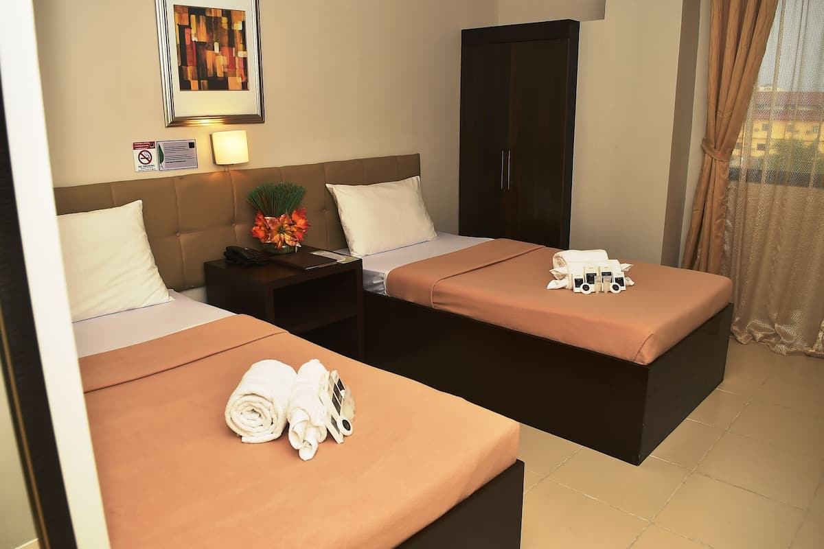 A hotel room with two beds, a dark wardrobe, a nightstand with a lamp, and a framed picture on the wall.