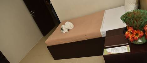 Una habitación de hotel con una cama, una mesita de noche con una lámpara, un jarrón con flores y un cartel sobre la mesita de noche.